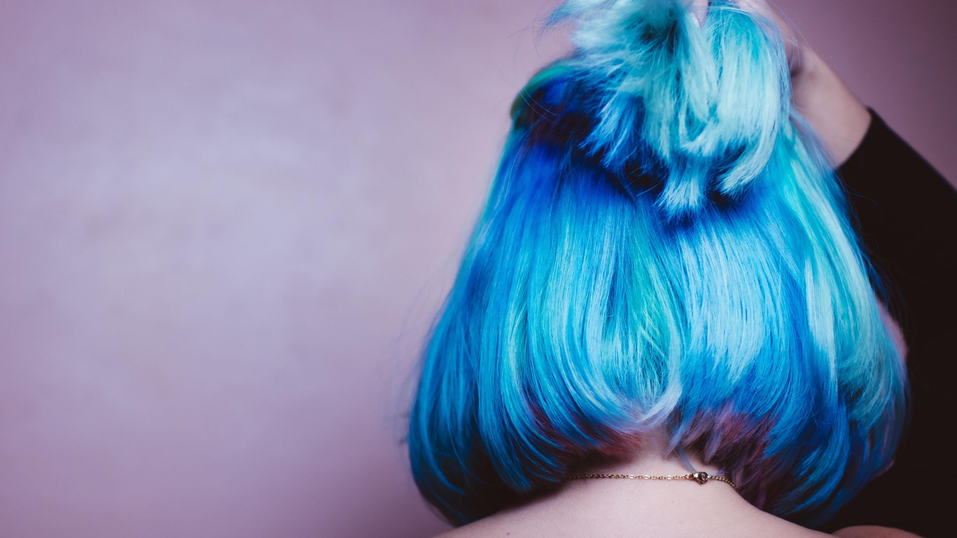 A woman with blue and green hair has her back to the camera